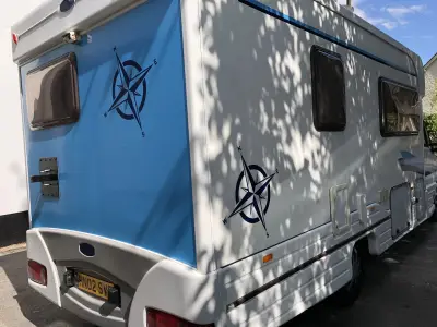 Rear of white motorhome with blue panel and navy nautical compass-rose vinyl graphics