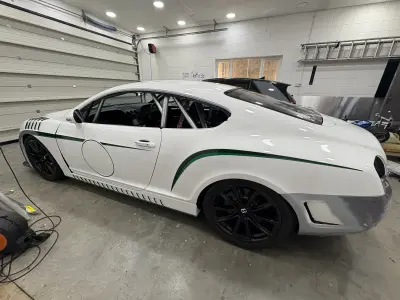 White Bentley Continental GT race car with green stripe racing livery in a workshop