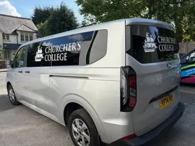 Silver Ford Tourneo Custom with white Churcher's College ship-crest window graphics along the side