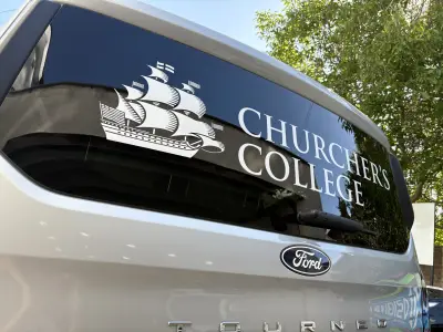 Close-up of white Churcher's College sailing-ship crest window graphic on silver Ford Tourneo