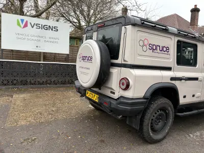 VSIGNS forecourt sign board beside sand-coloured Ineos Grenadier with Spruce fencing graphics