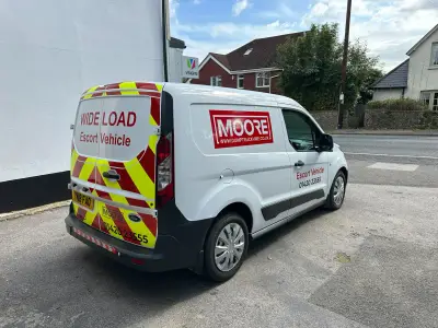 White Ford Transit Connect van, Moore Wide Load Escort Vehicle graphics and rear chevrons