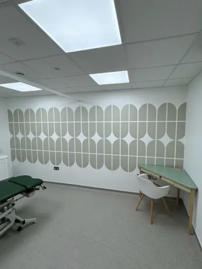 Treatment room with sage-green geometric wall vinyl behind a physio couch and desk