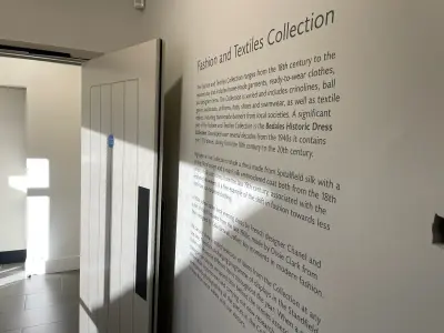 Museum wall with printed 'Fashion and Textiles Collection' text graphic beside a doorway