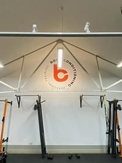 Personal training gym with orange Body Conditioning circular logo wall graphic above racks