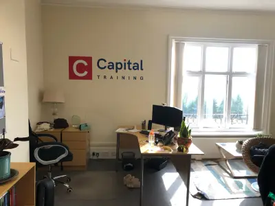 Office wall with red and navy Capital Training logo graphic beside a window
