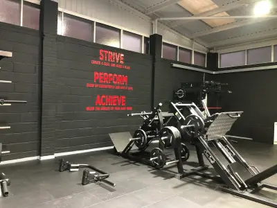 Gym with red Strive, Perform, Achieve wall lettering above leg-press machines