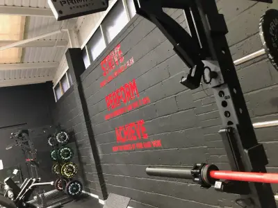 Gym grey wall with red Strive, Perform, Achieve vinyl lettering and weight plates