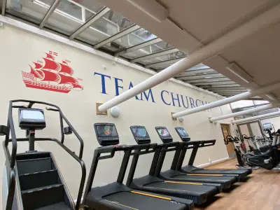 Gym wall with red sailing-ship logo and blue Team Churcher's lettering above treadmills