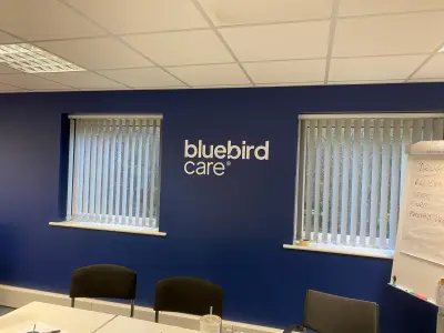 Office wall painted navy with white Bluebird Care logo between two blinded windows