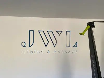 Gym wall with blue JWL Fitness & Massage logo graphic beside a rowing machine