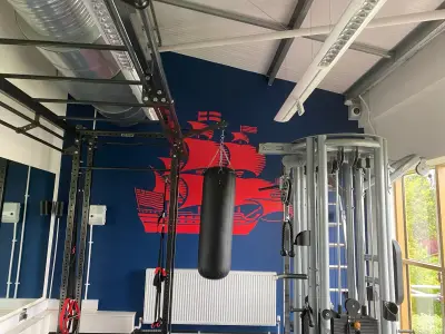 Gym with red sailing-ship graphic on navy wall behind a punchbag and cable machine