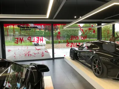 Black McLaren P1 showroom with Help Me and No One Leaves blood-splatter Halloween window graphics