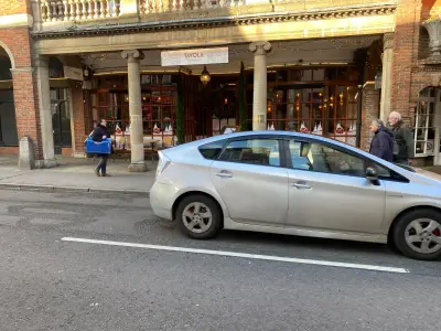 Silver Toyota Prius passing Tavola restaurant with fascia sign and festive window graphics