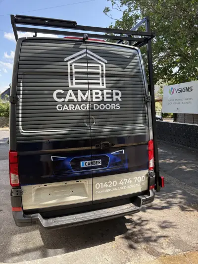 Rear of grey Camber Garage Doors wrapped van showing white logo and website, VSigns board behind