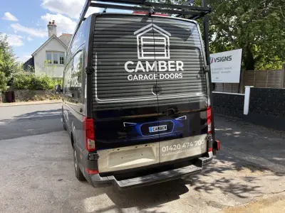 Rear view of grey Camber Garage Doors wrapped van parked by a VSigns forecourt sign
